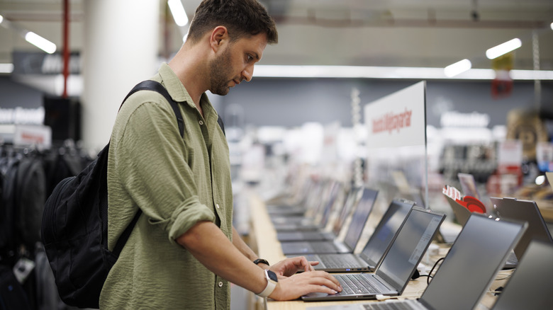 A male shopper in a computer store uses one of many laptops on display.