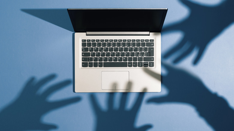 A laptop surrounded by shadows of hands seemingly trying to grab it.