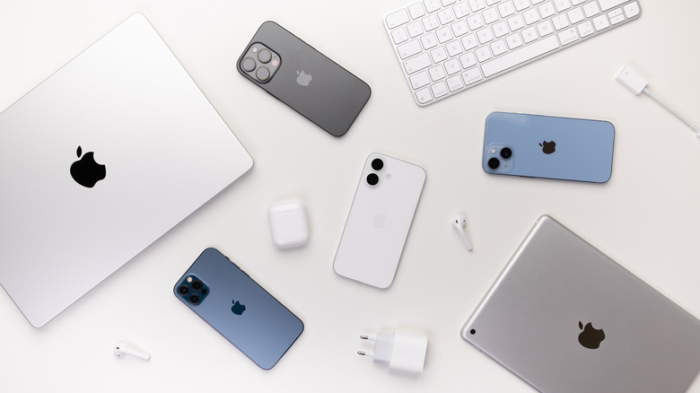MacBook, AirPods, three iPhones, an iPad, a charging cable and adapter, and an Apple keyboard placed on a table
