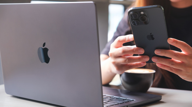 Person holding an iPhone with a MacBook and coffee mug kept on the table in the front