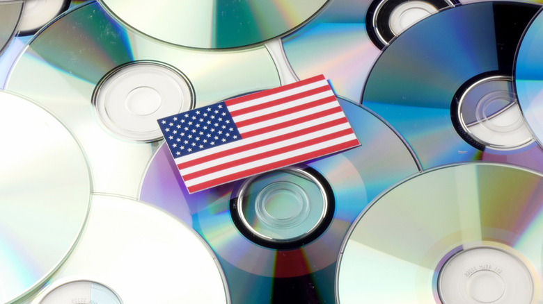 A small flag of America sits on top of several physical media discs that take up the surface of the image