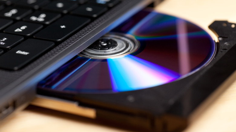 A Blu-ray disc sitting in the CD/DVD tray of a laptop, the disc drive is about halfway open, and some of the black laptop can be seen