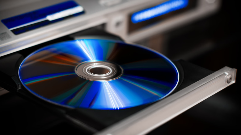 A blue compact disc sits in the tray of a DVD and/or Blu-ray player, the device itself is heavily blurred as the image focuses on the disc