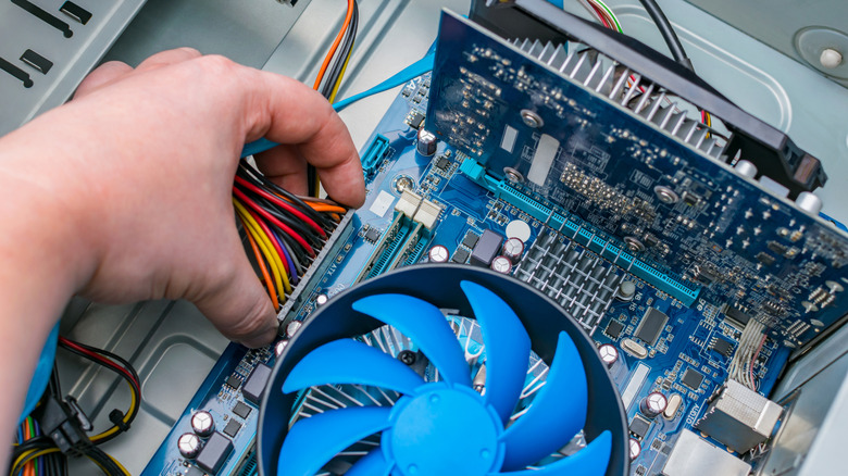 a person checking inside a computer with a hand near a fan and wires