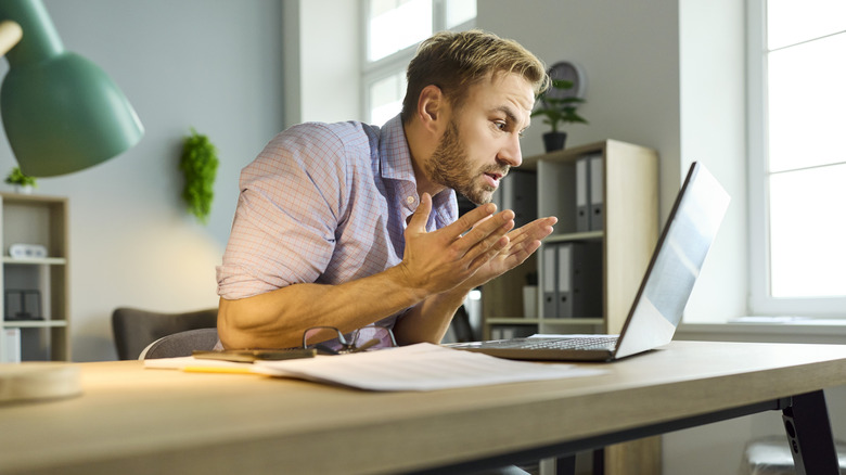 Person looking at a laptop placed on a table in frustration