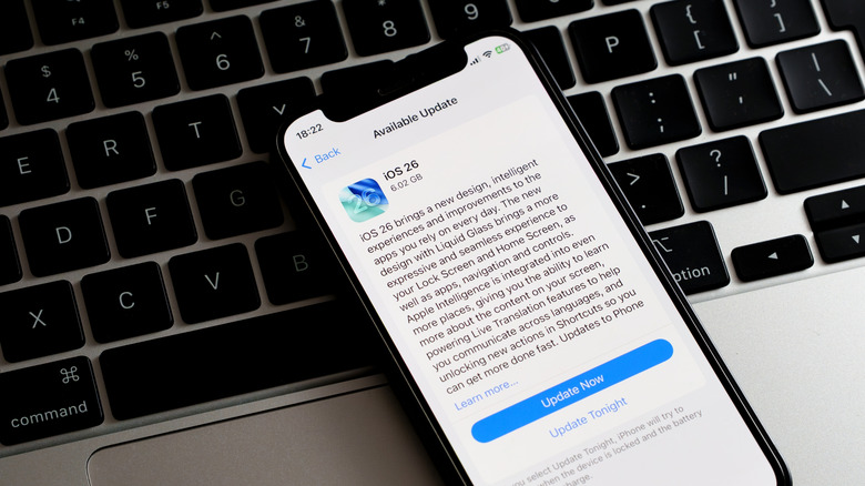 An iOS 26 update notice on an older iPhone model, set on top of a laptop keyboard.