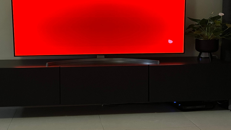 An OLED-type TV with a flat red screen showing signs of burnt in pixels, appearing as a dimming of pixels in the center of the screen