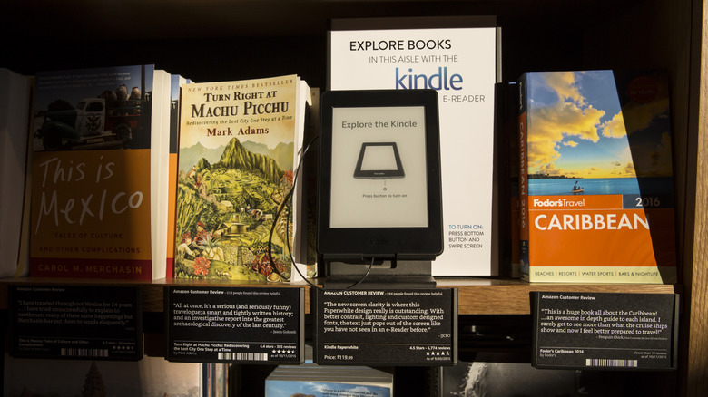 A Kindle alongside physical books on a bookshelf