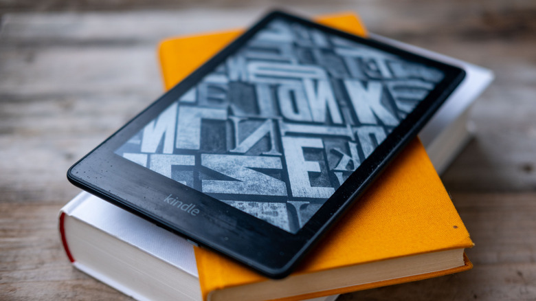A Kindle Paperwhite on top of a stack of books on a wooden surface