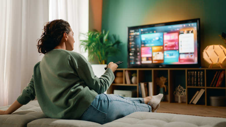 Woman using remote control while watching smart TV interface in living room