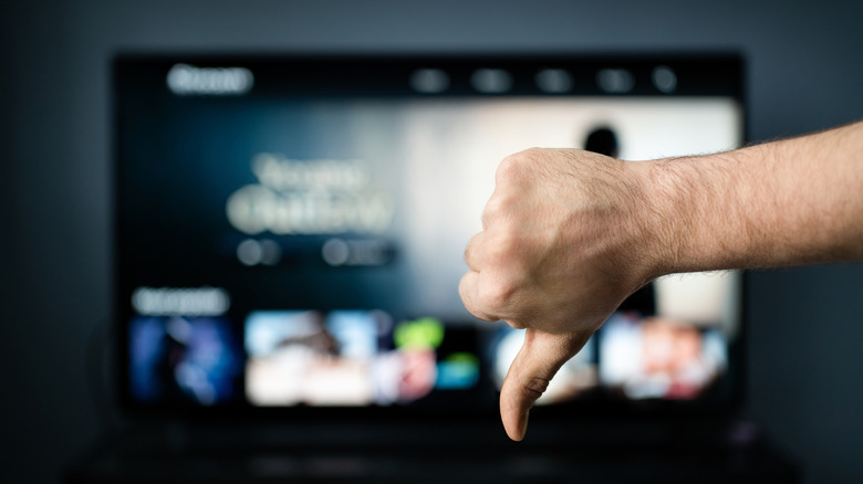 Hand giving thumbs down in front of blurred smart TV streaming interface