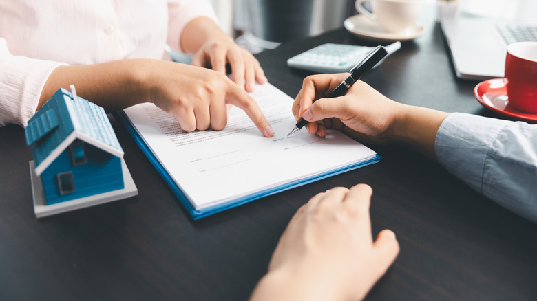 Person signing paperwork at a table beside a small house model.