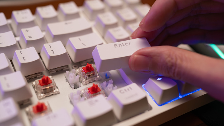 Person holding keyboard keycap over exposed keyboard switches
