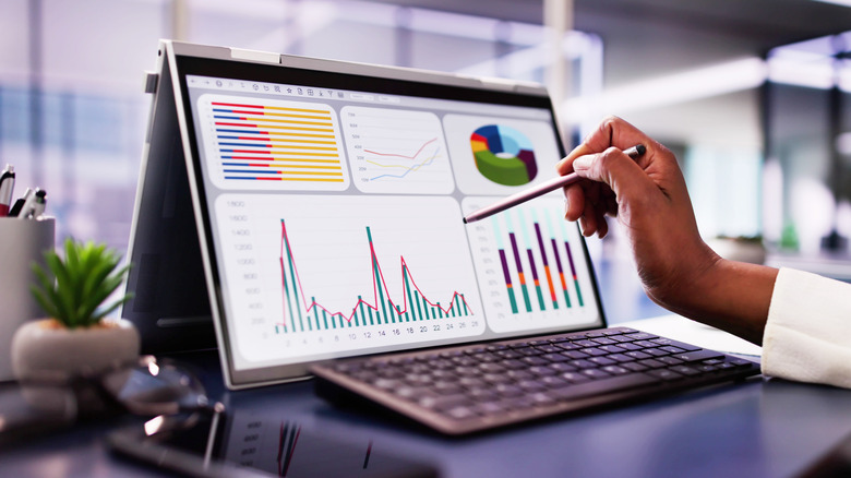 Person using a stylus on a touchscreen laptop displaying charts and graphs.