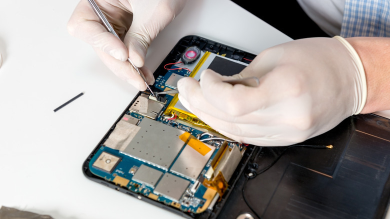 Technician repairing a tablet with precision tools while wearing gloves.