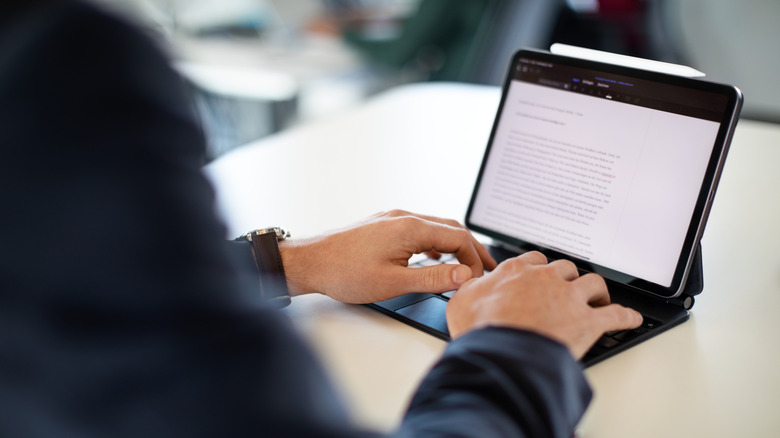 Person typing on a tablet with a keyboard case and stylus.