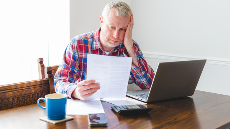 Person looking stressed while reviewing bills beside a laptop and calculator.