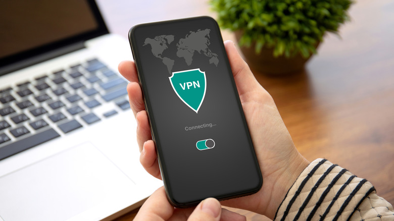 Person holding a smartphone showing a VPN connection screen beside a laptop.