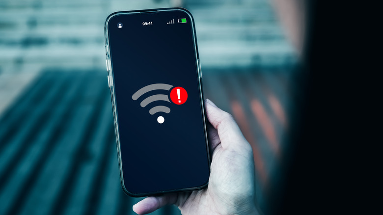 Person holding a smartphone showing a Wi-Fi warning icon on the screen.