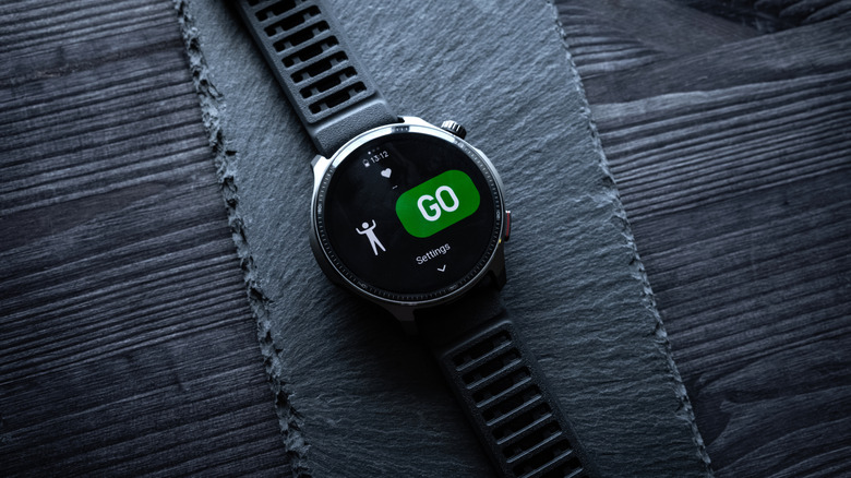 A black Amazfit Balance 2 XT displaying a large green GO button as the device sits on a black material