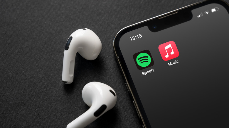 AirPods next to an iPhone showing the Spotify and Apple Music app icons.