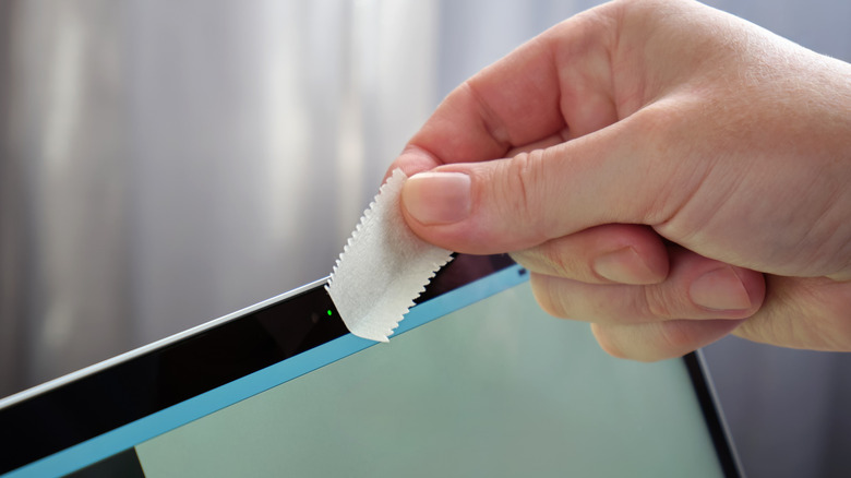 Hand putting a tape on the webcam area of a laptop screen.