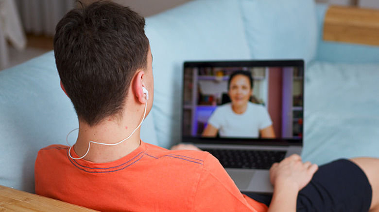 Person wearing earbuds and participating in a video call on a laptop while sitting on a couch.