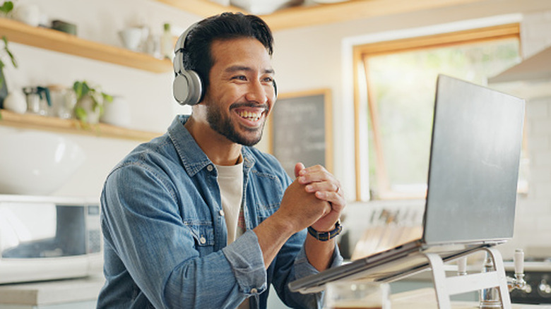 Smiling man wearing headphones during a video call on a laptop at home.