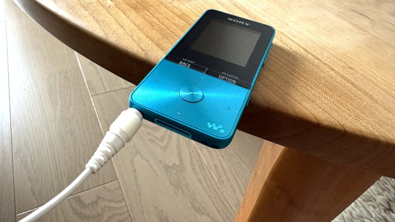 Wired earbuds connected to a music player that's teetering on the edge of a table