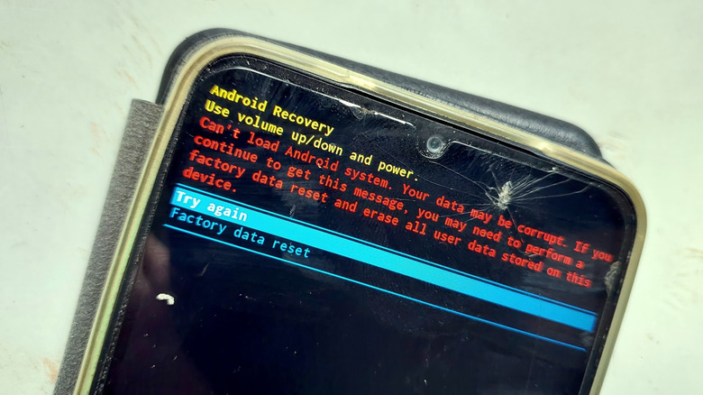 Close up of a broken phone with a cracked screen displaying Android's recovery mode with the factory reset option being prompted
