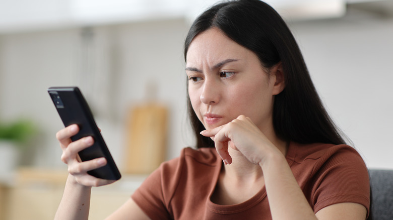 A woman looking at her phone with a stressed expression on her face