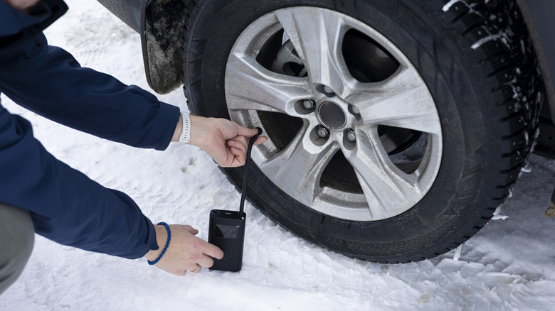A driver plugging a portable air pump into a tire.