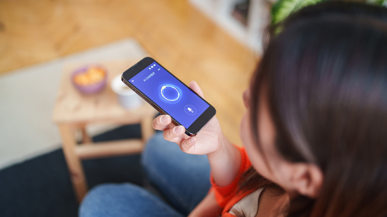 Woman using a smartphone voice assistant app while sitting at home.