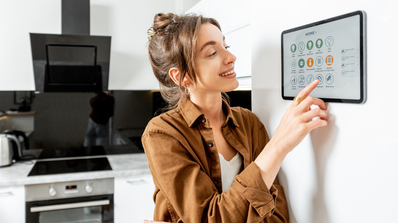 Woman using a wall-mounted smart home control panel in a kitchen.
