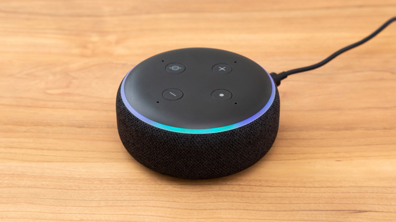 Amazon Echo Dot smart speaker with a blue light ring plugged in on a wooden table.