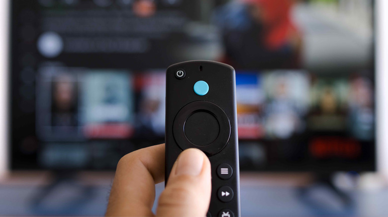 Hand holding a streaming remote in front of a blurred Smart TV screen.
