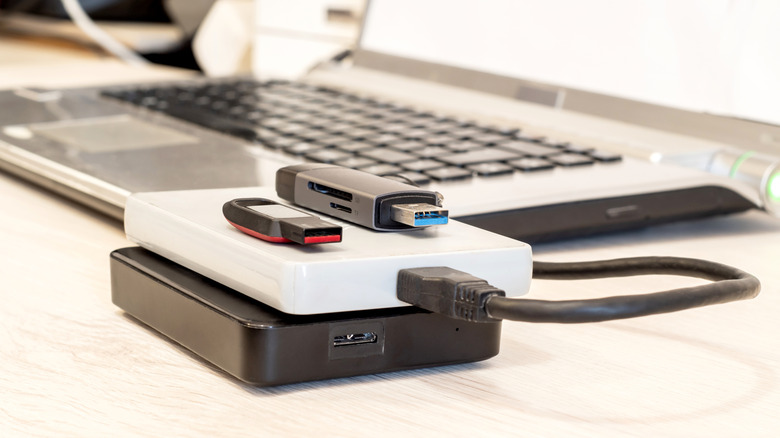 External drives and thumb drives stacked up next to a laptop.