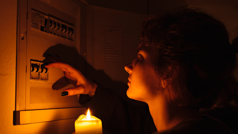 A person with a candle checking a fuse box in a power outage.