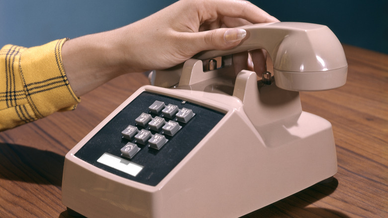 A hand picking up the receiver of a pink touch-tone phone