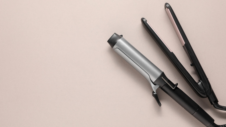 a hair straightener and curling iron on a beige background