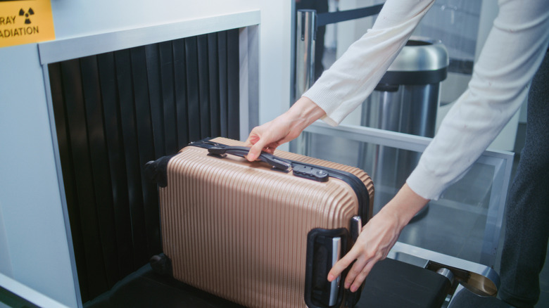 person placing a carry-on suitcase into a scanner