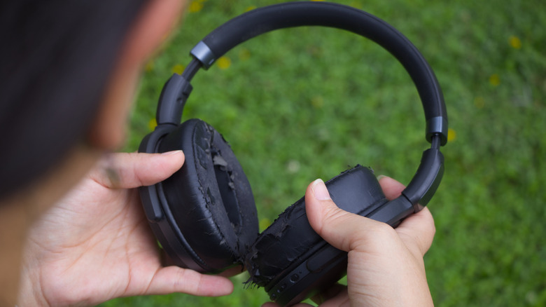 A person holding a pair of wireless headphones with damaged earpieces