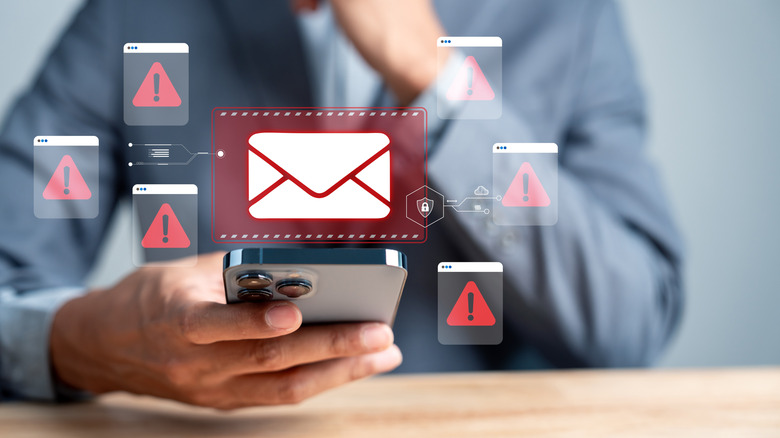 Close up of someone holding a smartphone with an email icon surrounding by warnings.