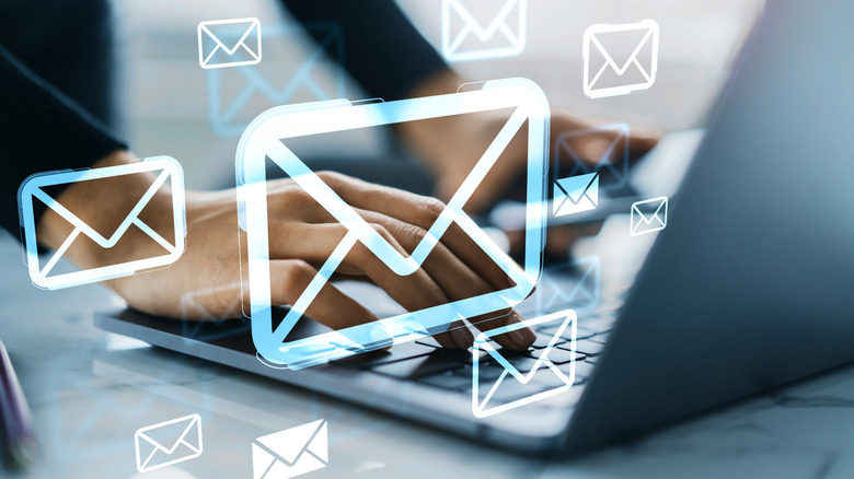 Close up of hands typing on a laptop with email icons over it