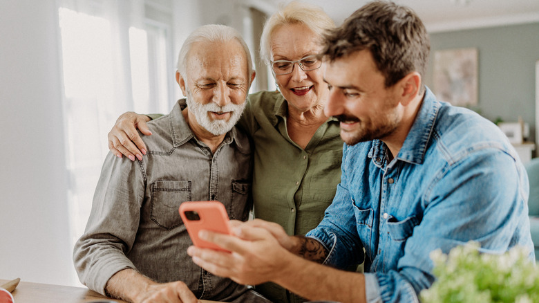 A young man with an elderly couple, showing them something on his phone.