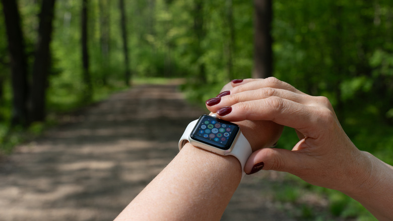 A wrist on a trail with an Apple Watch, a hand touching the button.