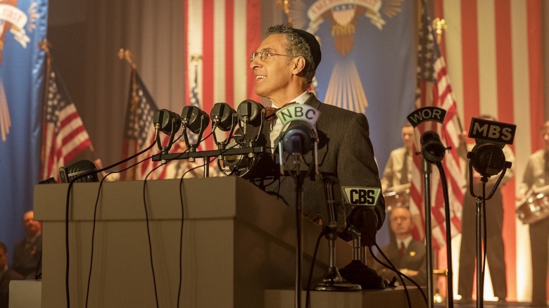 Rabbi Lionel Bengelsdorf smiling while standing at a press podium in "The Plot Against America."