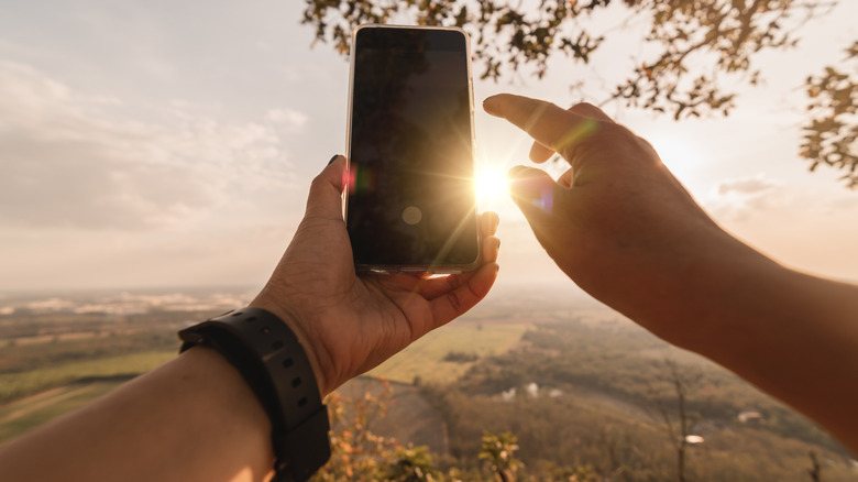 person capturing sunset on phone