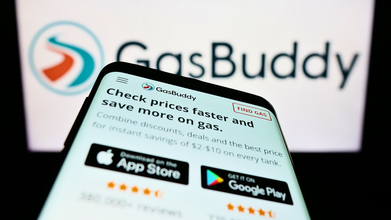 GasBuddy displayed on a phone and on a vehicle display in the background