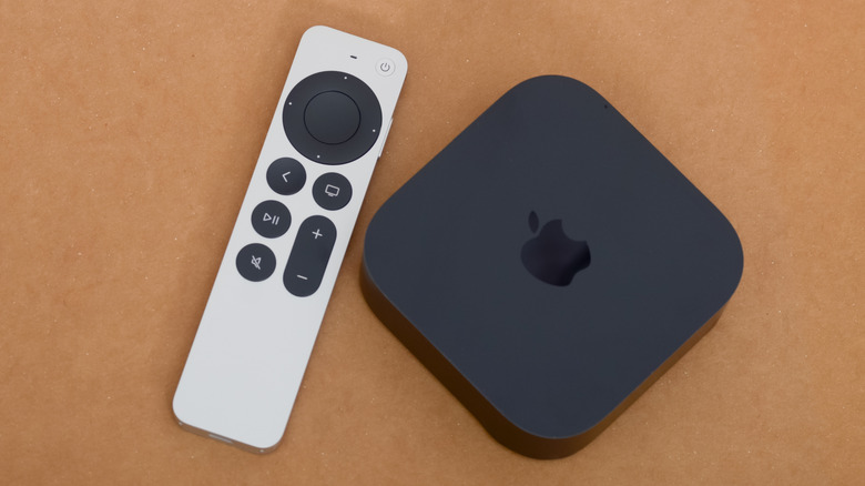 A black Apple TV 4K sitting next to its remote on top of a wooden table